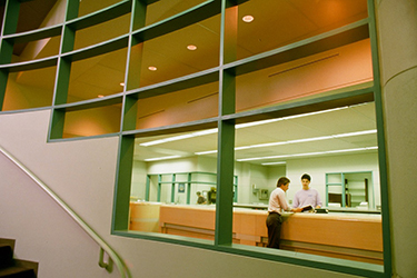 Photograph: A view of the Circulation Desk taken through the metal grating along the stairwell by the main entrance.